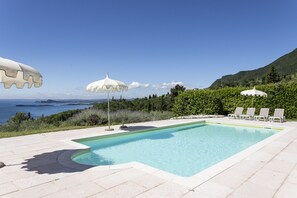 Une piscine entourée de verdure, avec des chaises longues et des parasols, offrant une vue sur la mer.