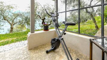 Ein Indoor-Hometrainer mit Blick auf eine Rasenfläche und Bäume durch große Fenster.