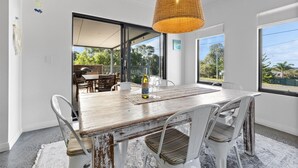 A dining area with a rustic wooden table, white chairs, and a woven pendant light.