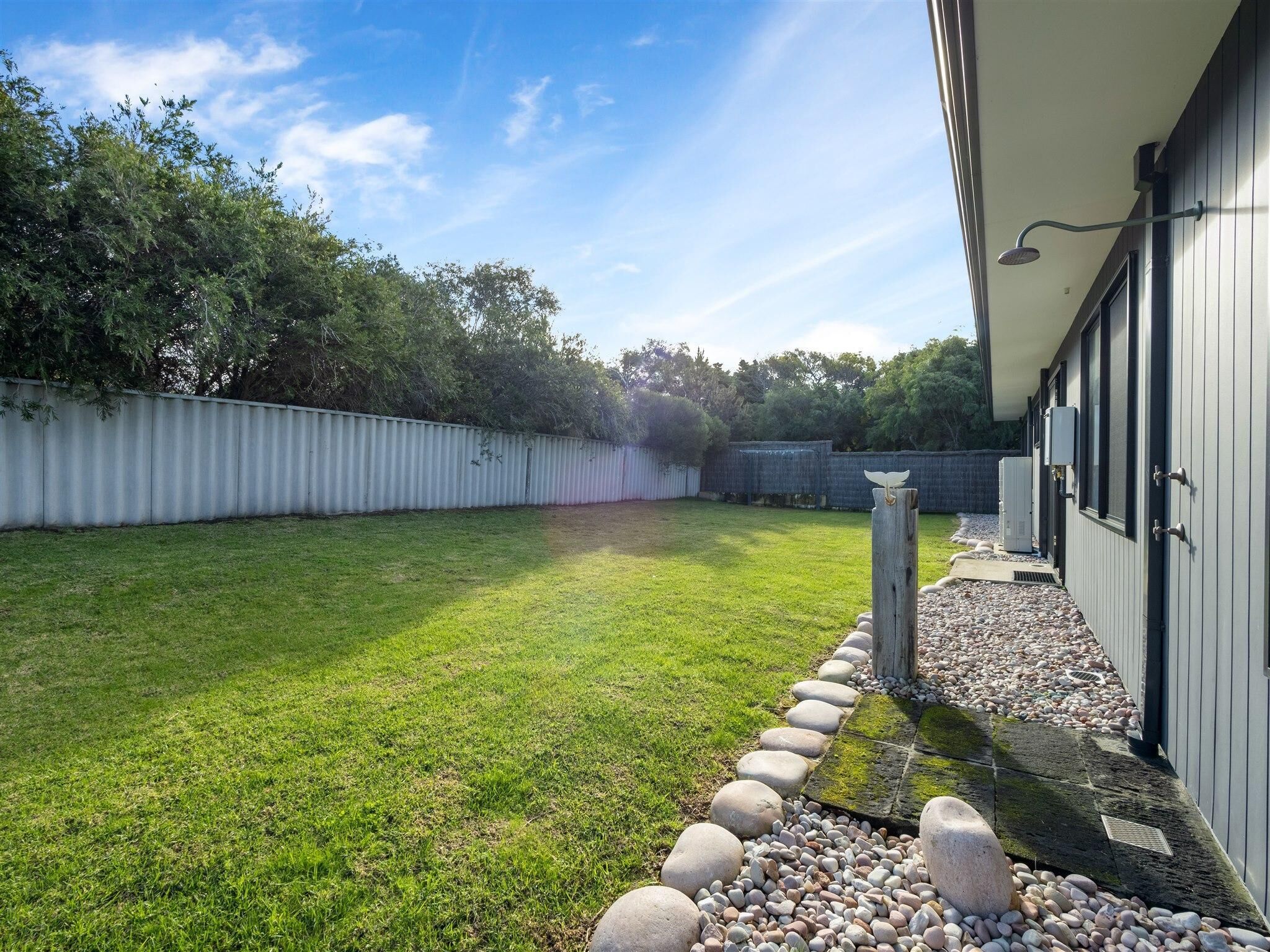 A backyard with a well-maintained lawn, a stone border, and a wooden post with a birdhouse.