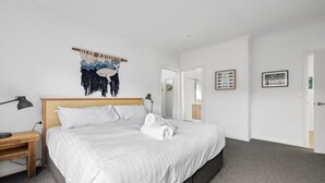 A modern bedroom with a large bed, a bedside table, a wall-mounted artwork, and a door leading to a bathroom.
