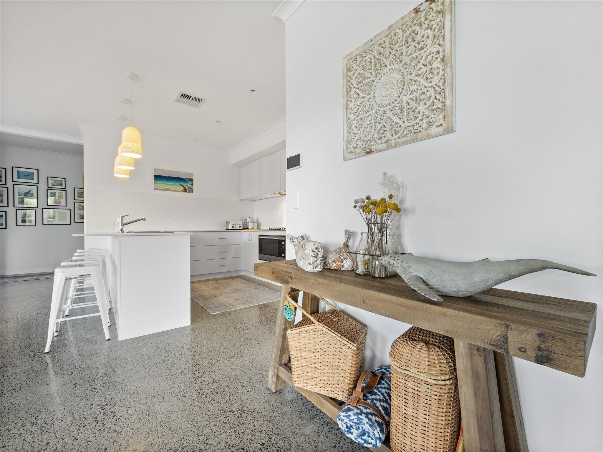 Una cocina moderna con armarios blancos, una isla central y un banco de madera con cestas.