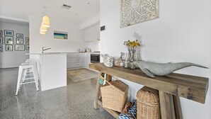 A modern kitchen with white cabinetry, a central island, and a wooden bench with baskets.