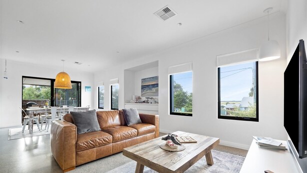 A modern living room with a leather sofa, a wooden coffee table, and large windows offering views of the outdoors.