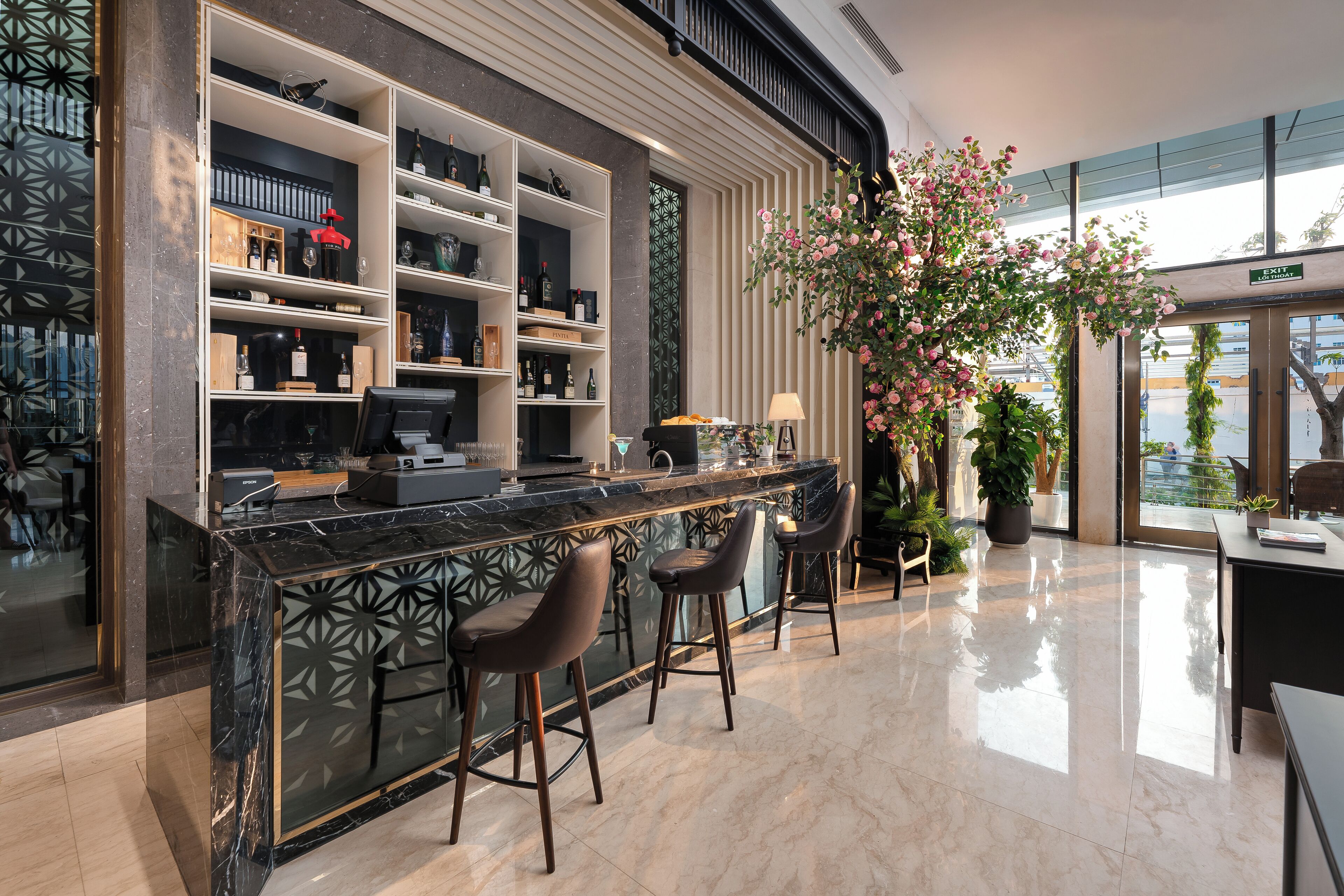 Un área de bar moderna con encimera de mármol, taburetes y estantes con botellas y vasos.
