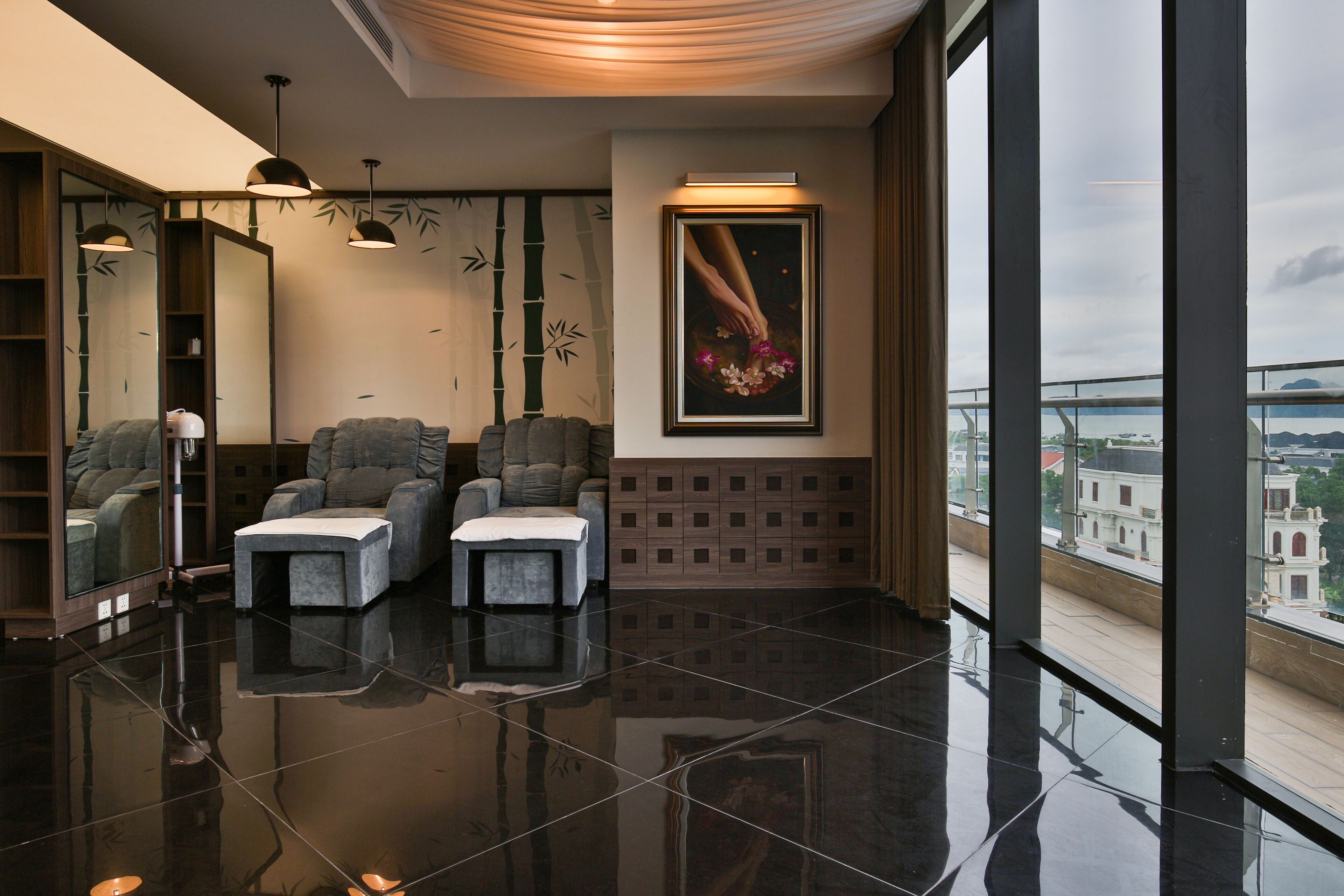 A modern lobby with a large mirror, two gray armchairs, a small table, and a framed artwork above a wooden cabinet.