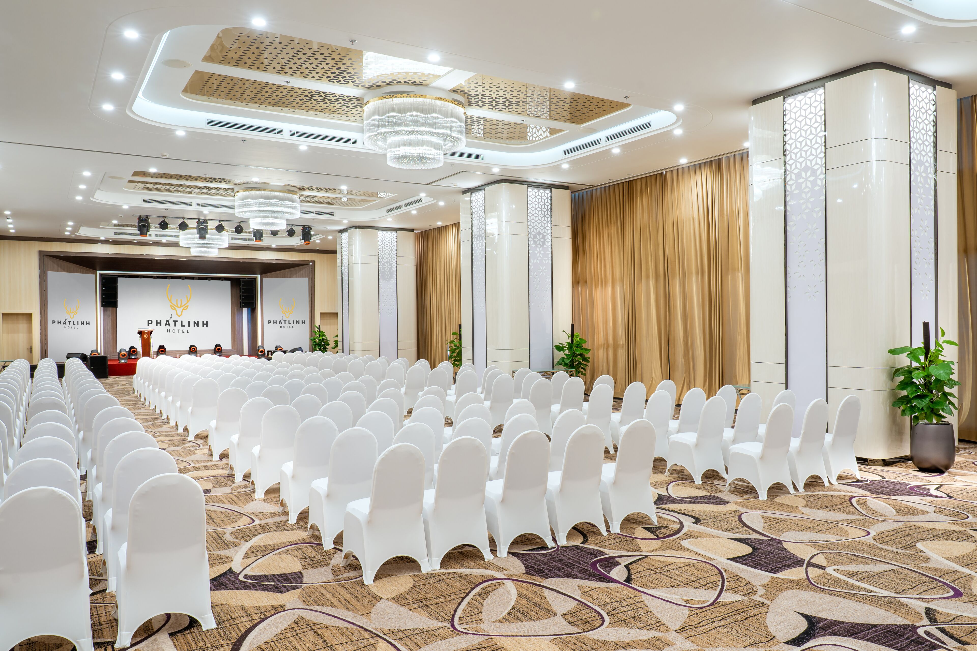 A conference room with rows of white chairs, a stage with a podium, and a chandelier.