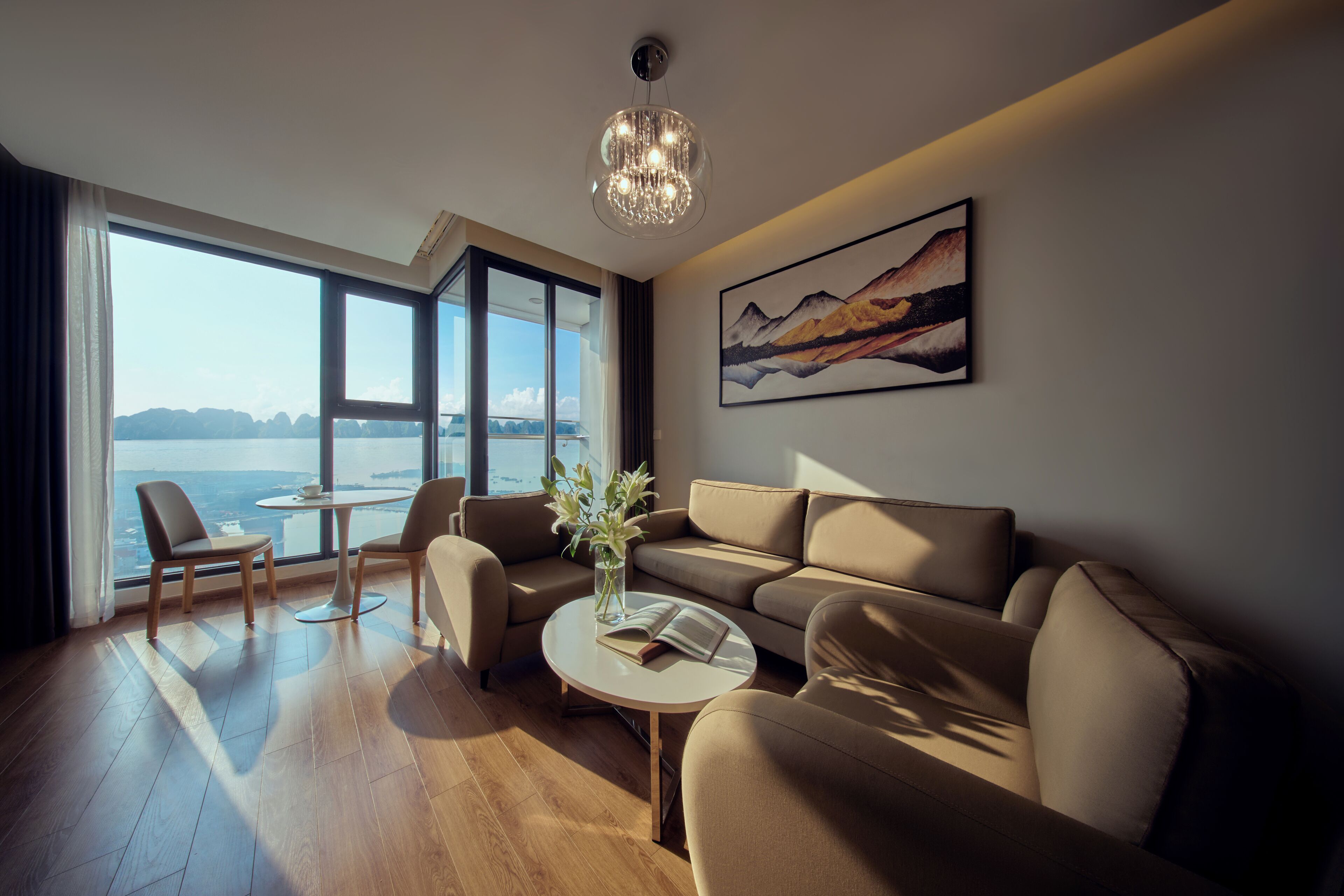 A modern living room with a sofa, chairs, a coffee table, and a view of the sea through large windows.