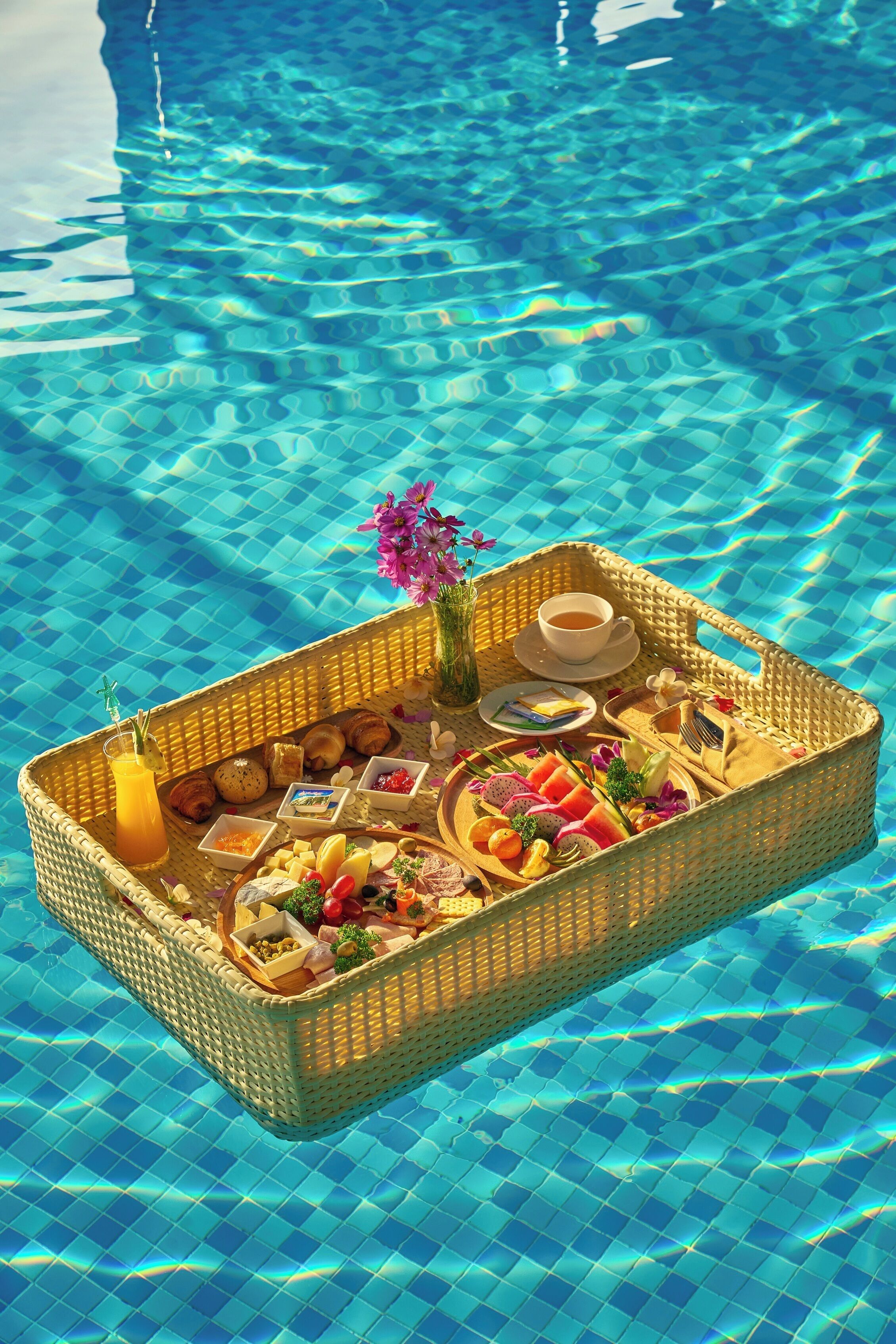 A floating basket with food and drinks on a pool.