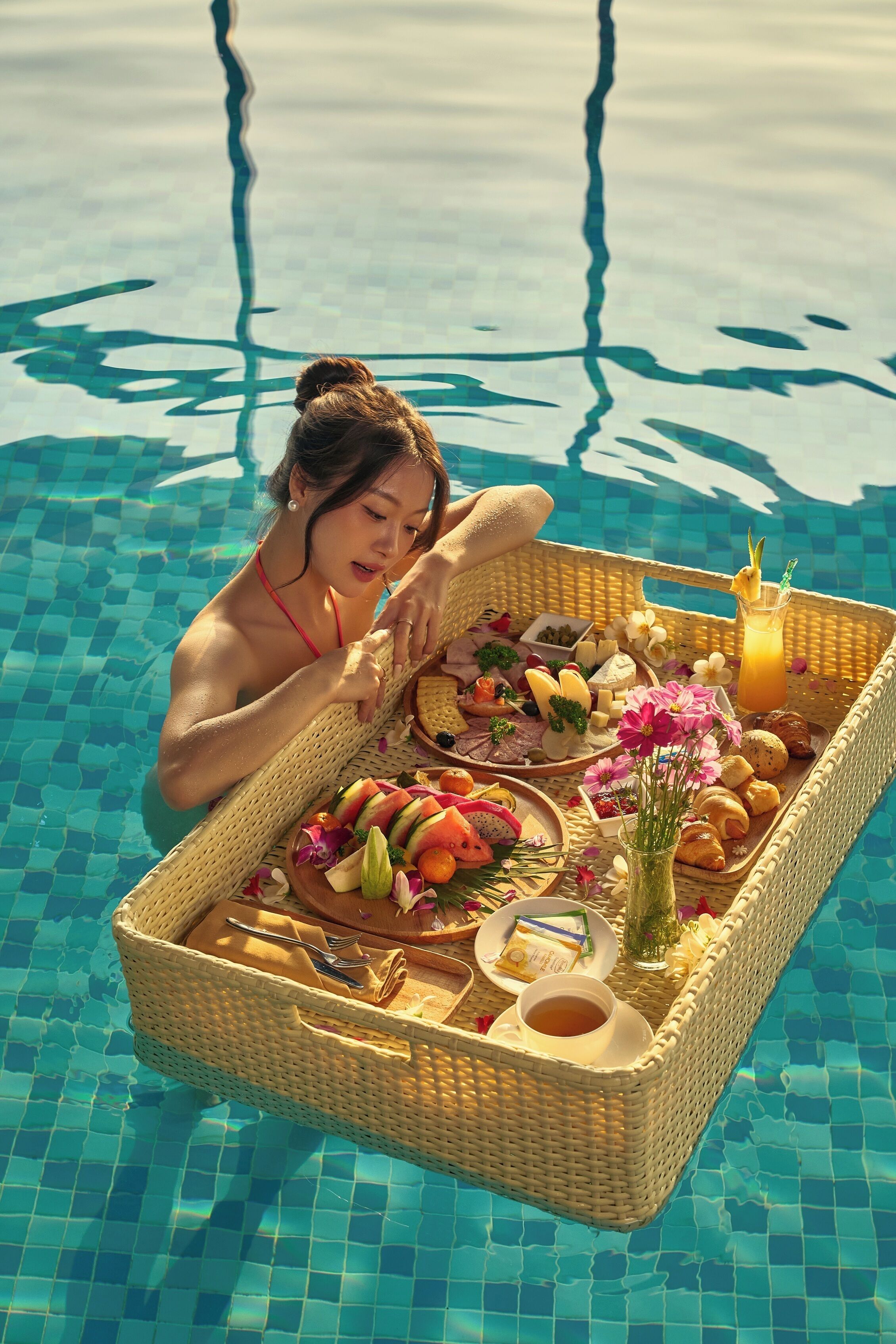 Una persona en una piscina con una bandeja de mimbre que contiene comida y bebidas.