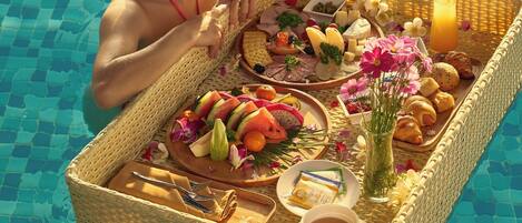 A person in a pool with a wicker tray containing food and drinks.