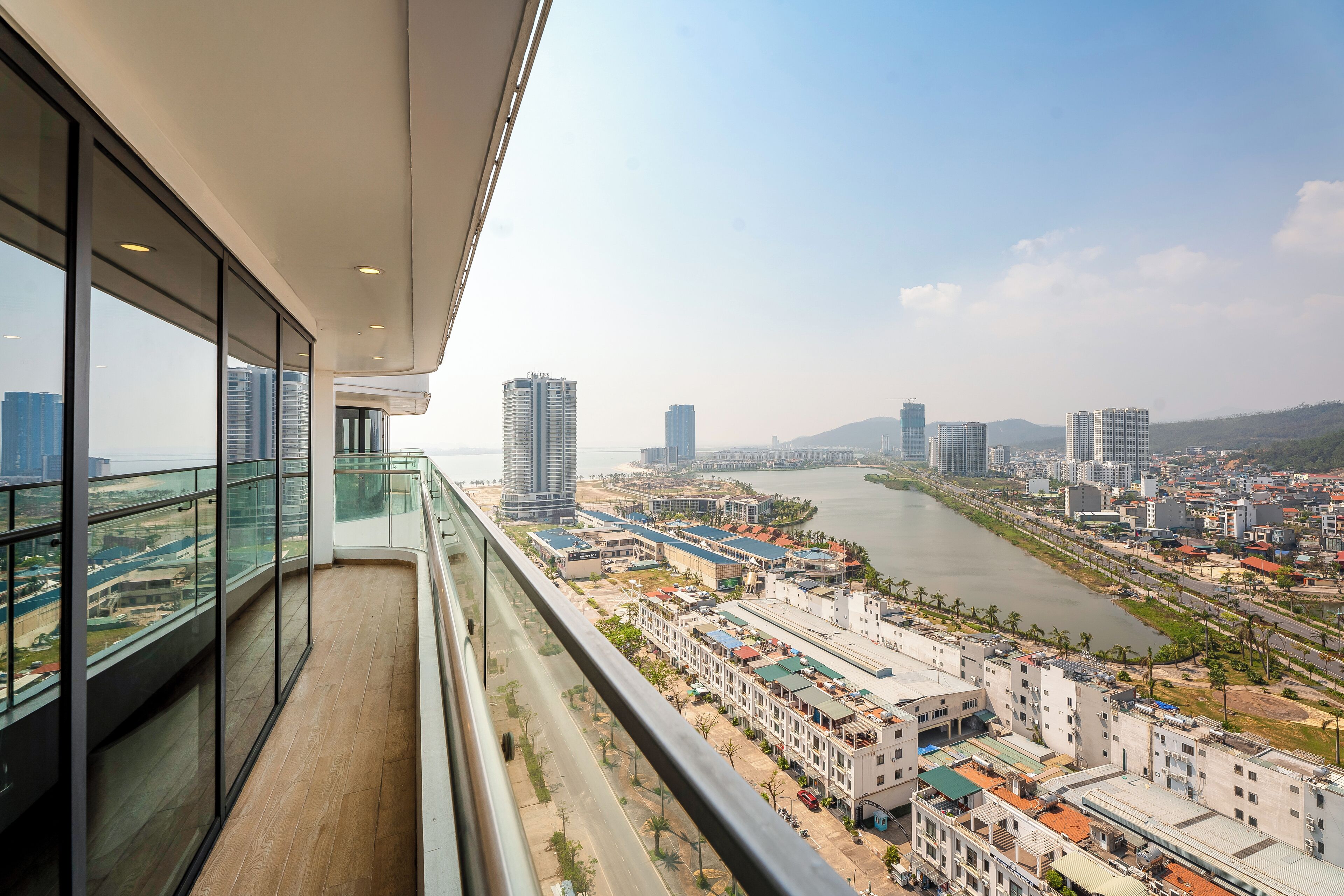 A high-rise building with a balcony overlooking a cityscape, including a river and various buildings.