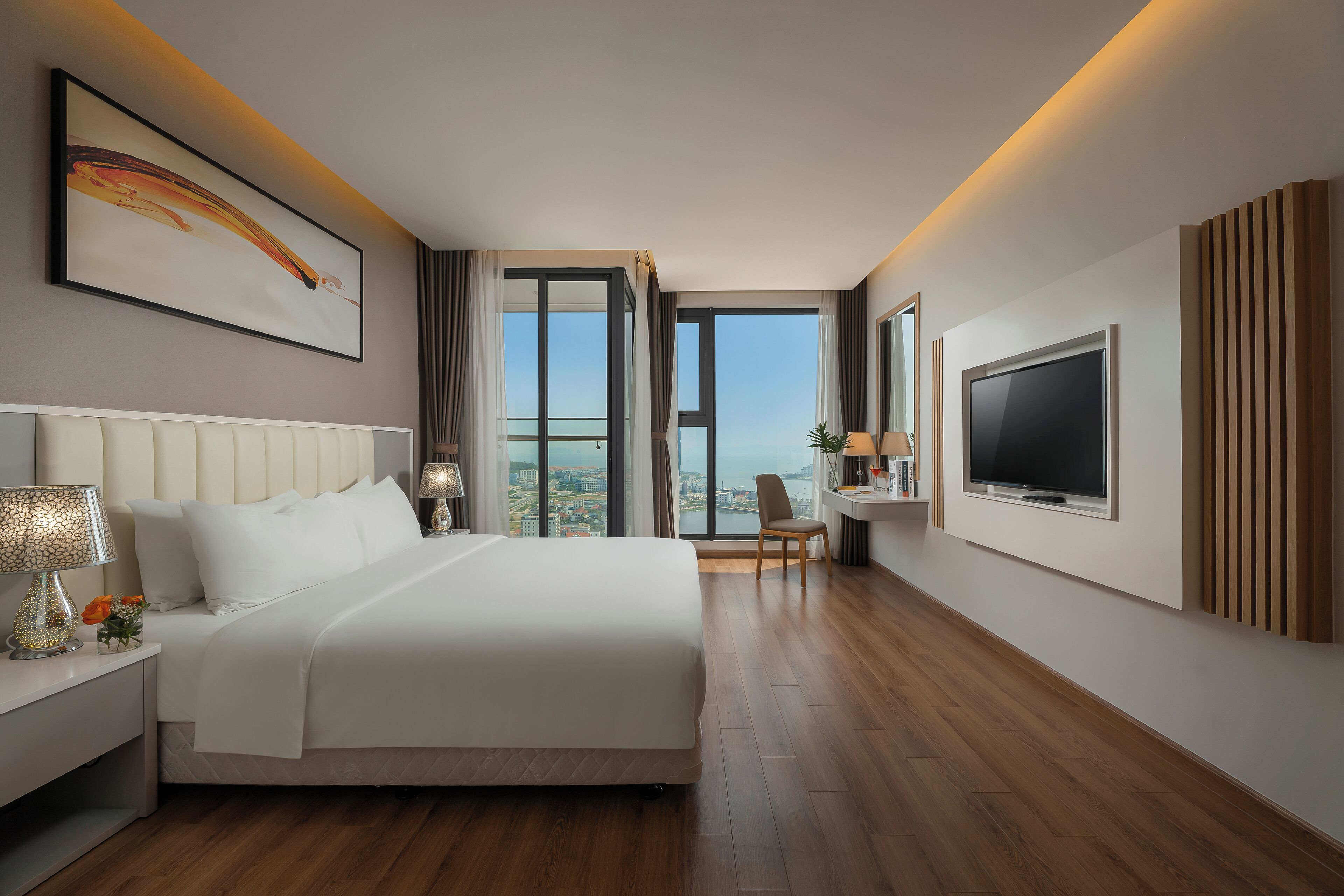A modern hotel room with a large bed, a desk, a TV, and a city view.
