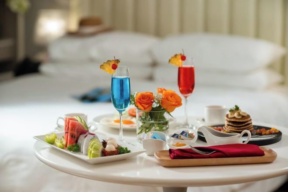 A breakfast setup with a variety of food items and drinks on a tray, including a plate with sliced fruit, a small bowl of eggs, and a stack of pancakes.