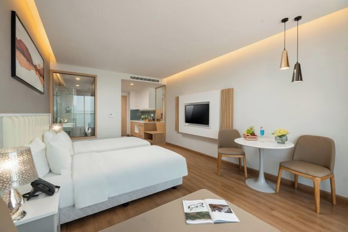 A modern hotel room with a large bed, a desk, a TV, and a small dining area.