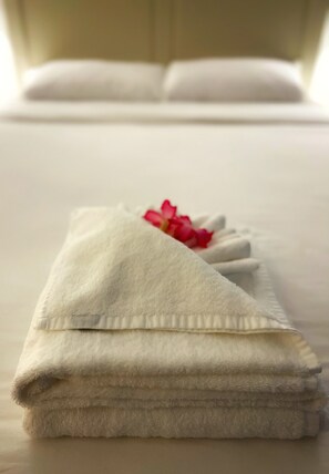 A neatly folded white towel with a pink flower on a bed.
