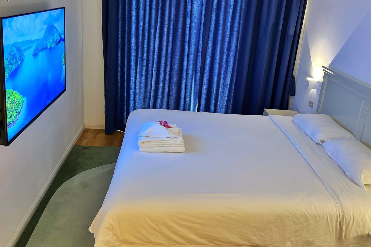 Ein Hotelzimmer mit einem Bett, einem an der Wand befestigten Fernseher und einem Vorhang.