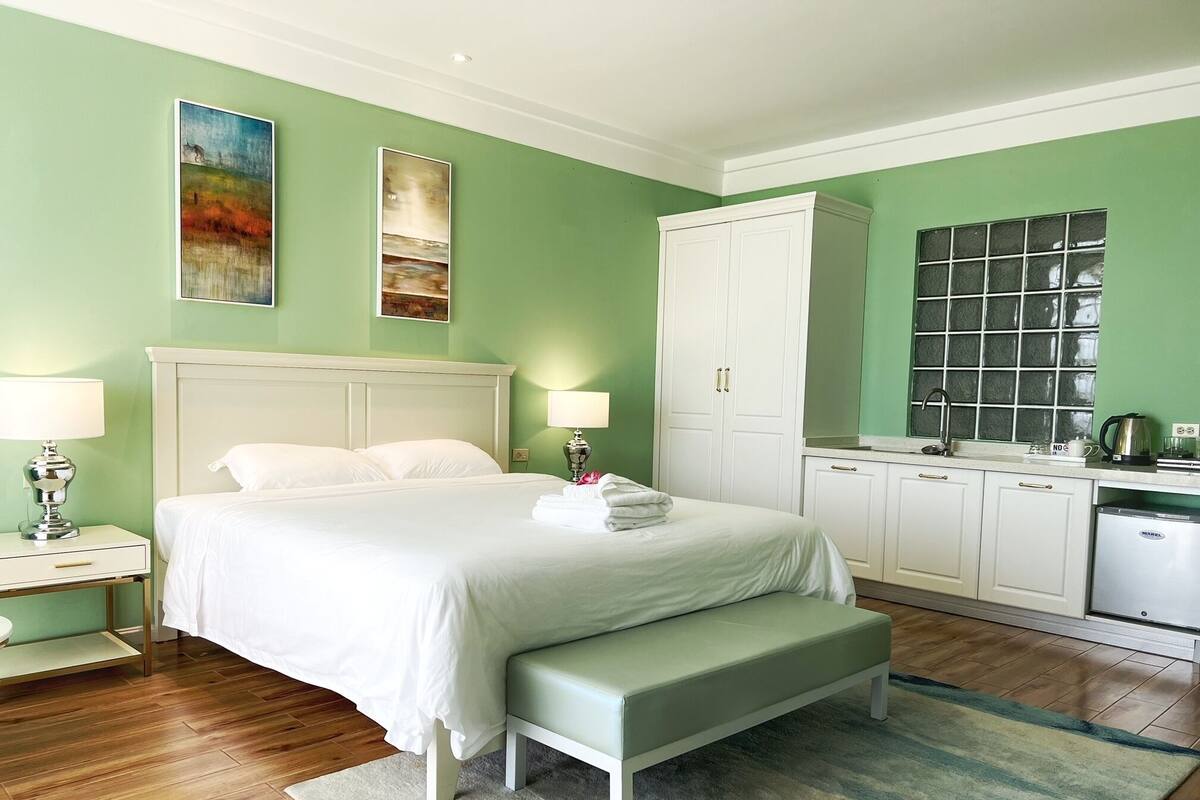 Ein Hotelzimmer mit Bett, Nachttischen, einer Bank, einer Küchenzeile und Bildern an den Wänden.