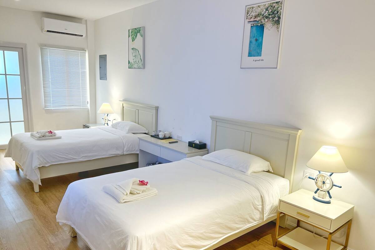 Ein Hotelzimmer mit zwei Betten, einem Schreibtisch, einem Stuhl und einem kleinen Tisch mit Lampe.