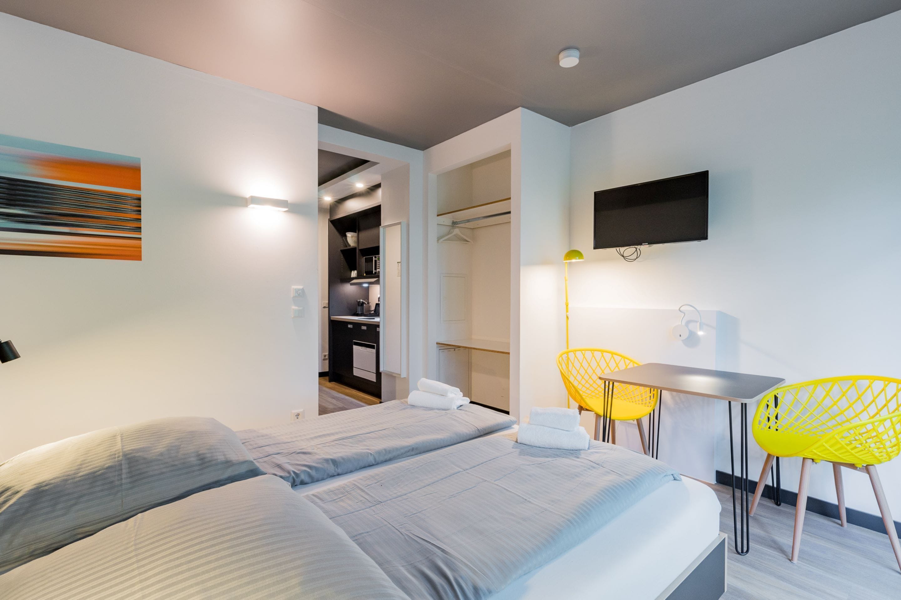 Habitación de hotel moderna con cama, escritorio y silla. Hay un televisor montado en la pared y un perchero.