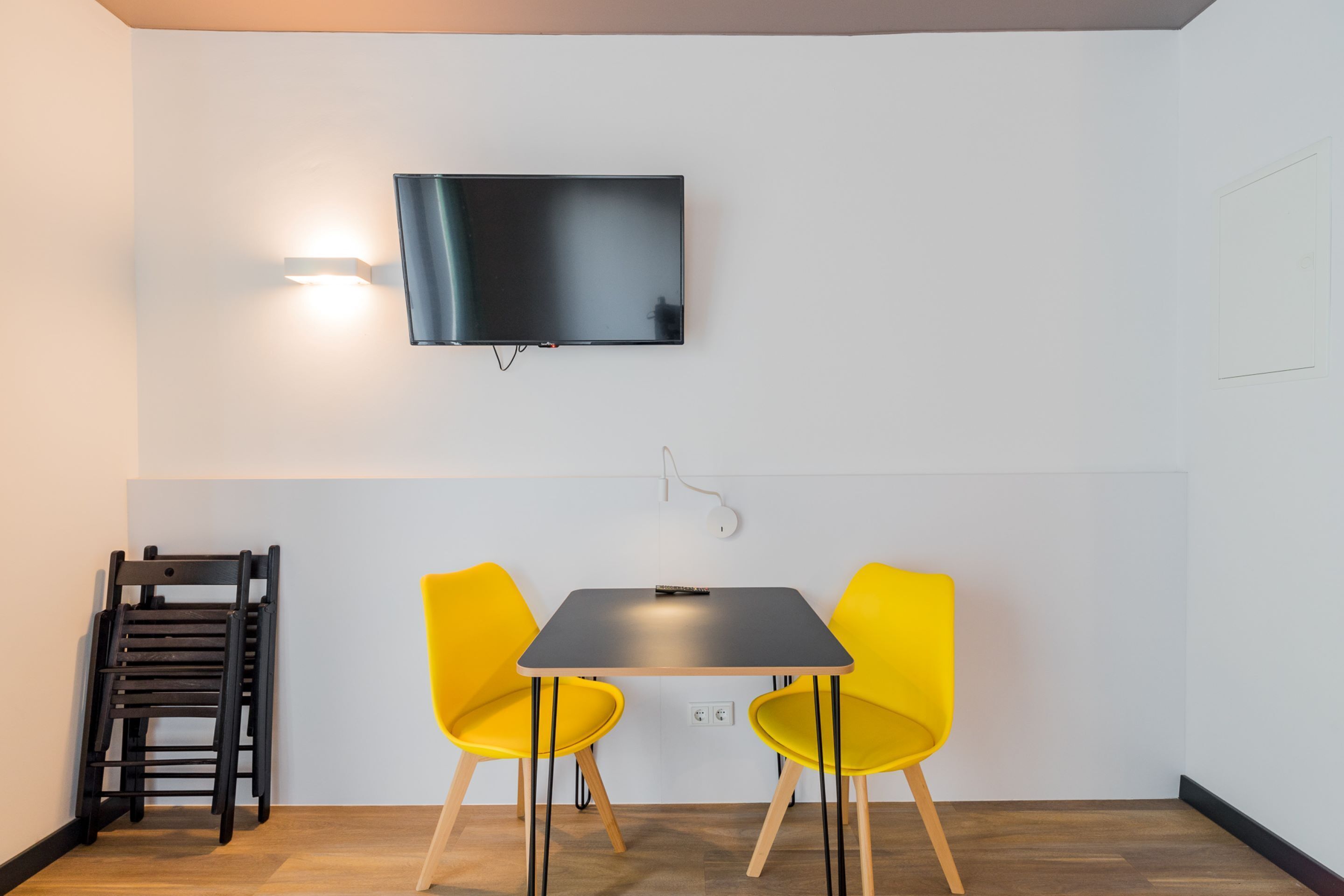 A modern room with a flat-screen TV mounted on the wall, a small table, and two yellow chairs.