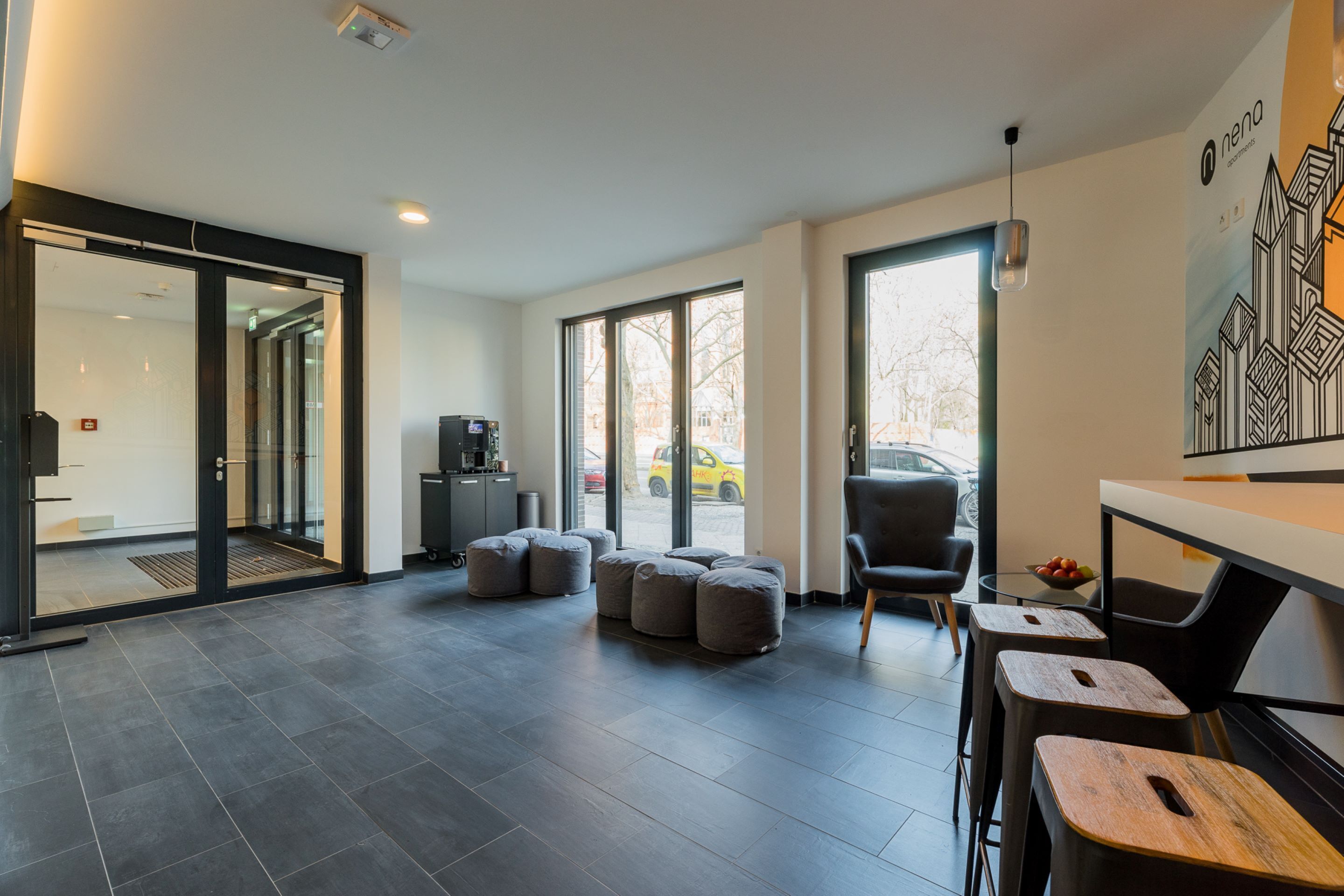 Un interior moderno con un espacio amplio abierto, una cafetera y una zona de estar con taburetes y una silla.