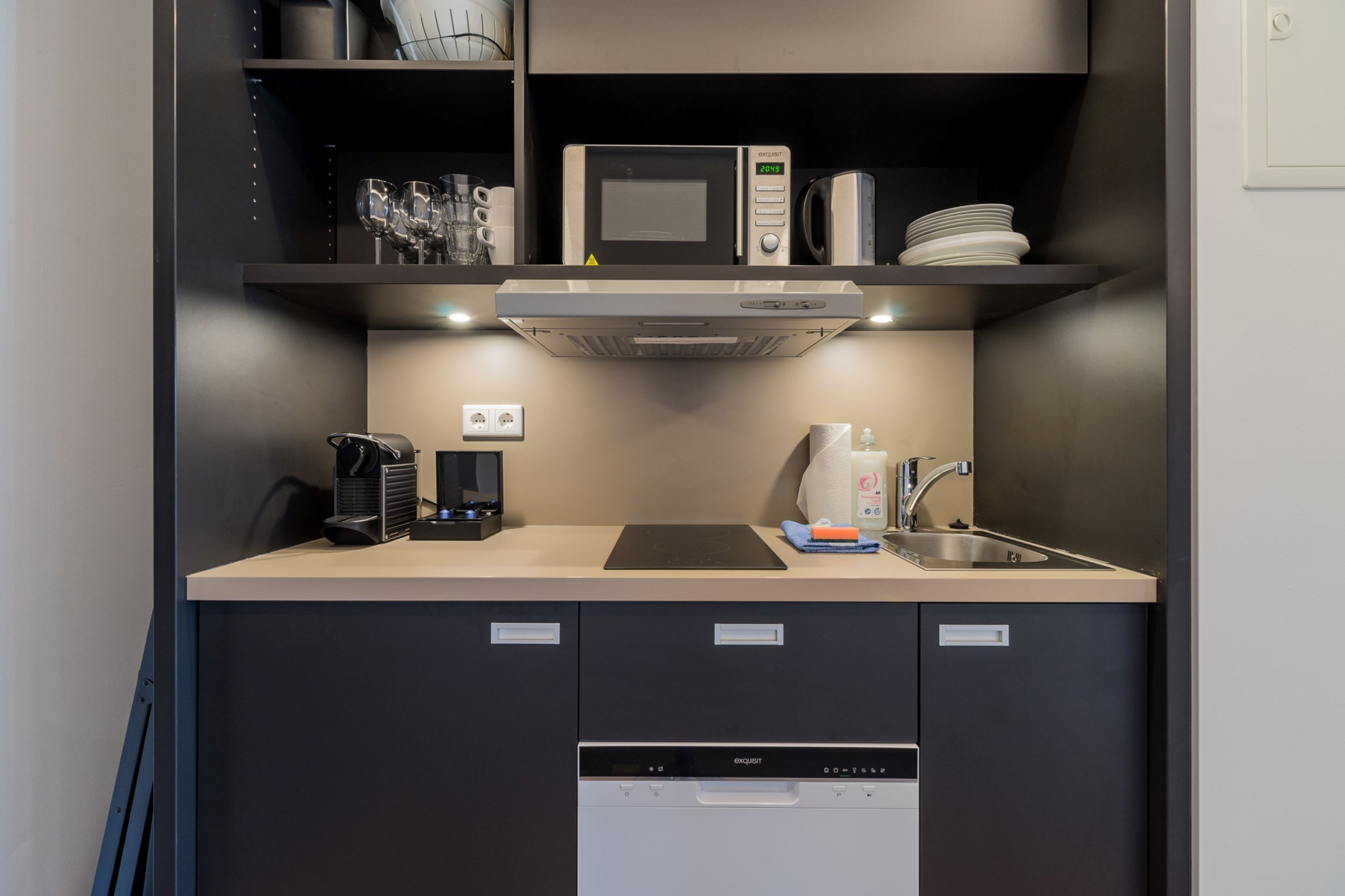 Una kitchenette compacta equipada con microondas, cafetera y lavabo.