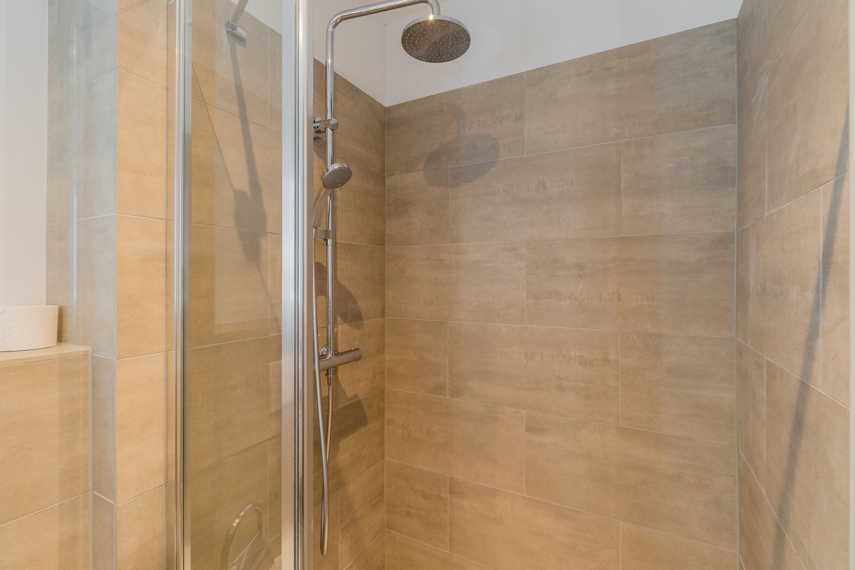 Eine Duschkabine mit Glaswänden, einer Handbrause und einem am Wand montierten Wasserhahn.