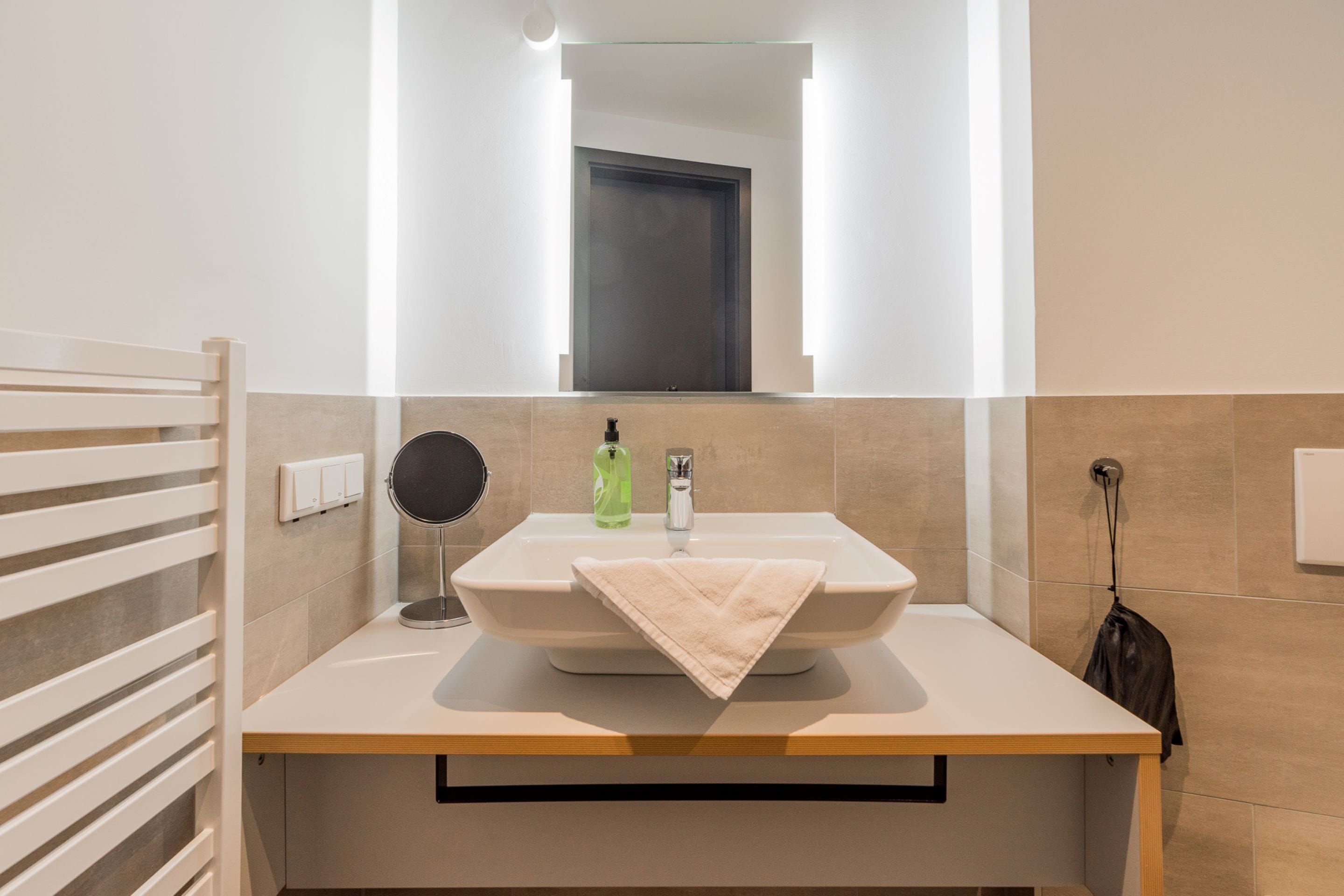 Une salle de bain avec un grand miroir, un lavabo, une serviette et un flacon de savon pour les mains.