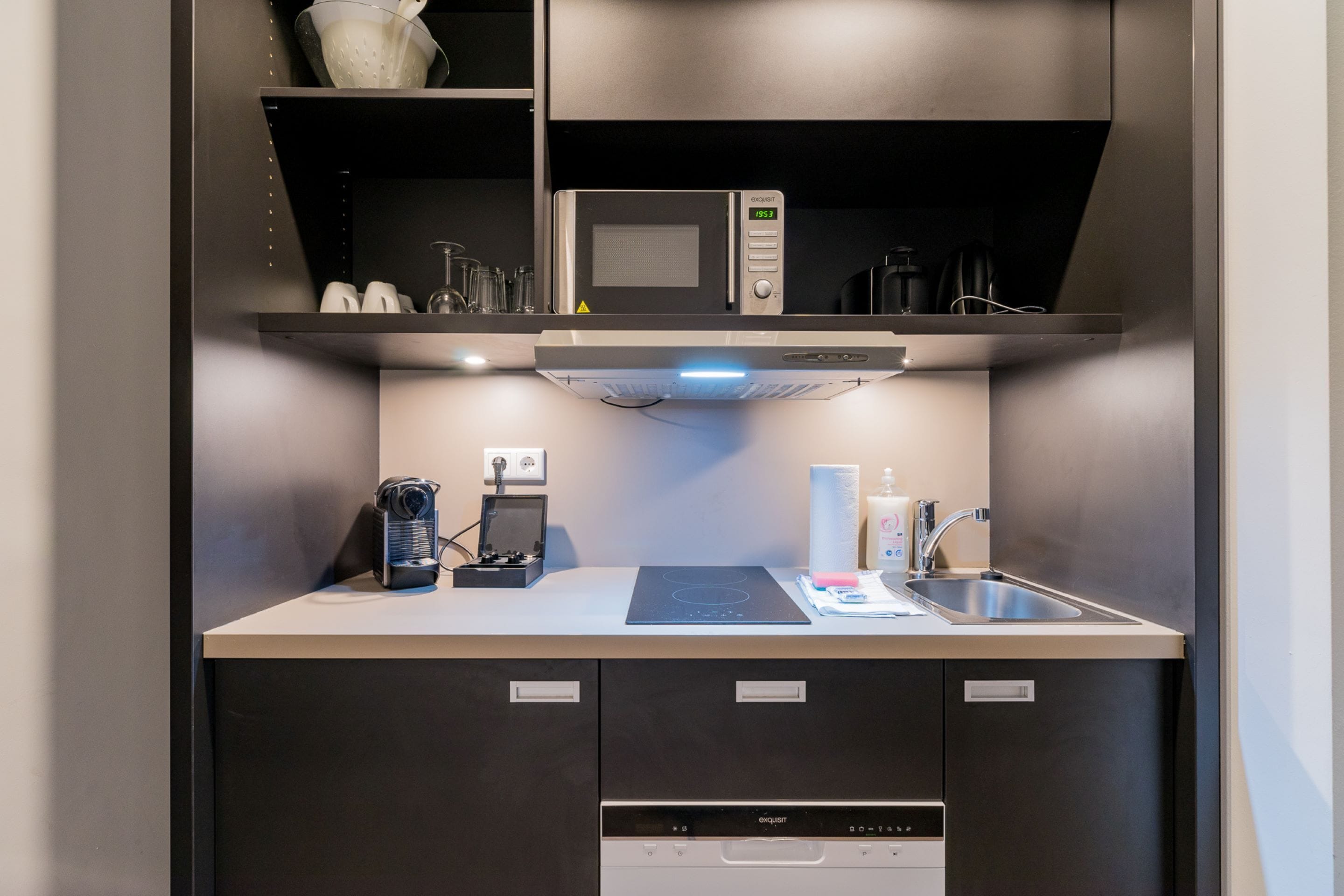 A compact kitchen with a microwave, coffee machine, and dishwasher.