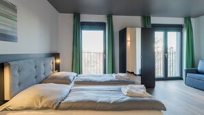 Habitación de hotel con dos camas, un sofá y un balcón con cortinas verdes.