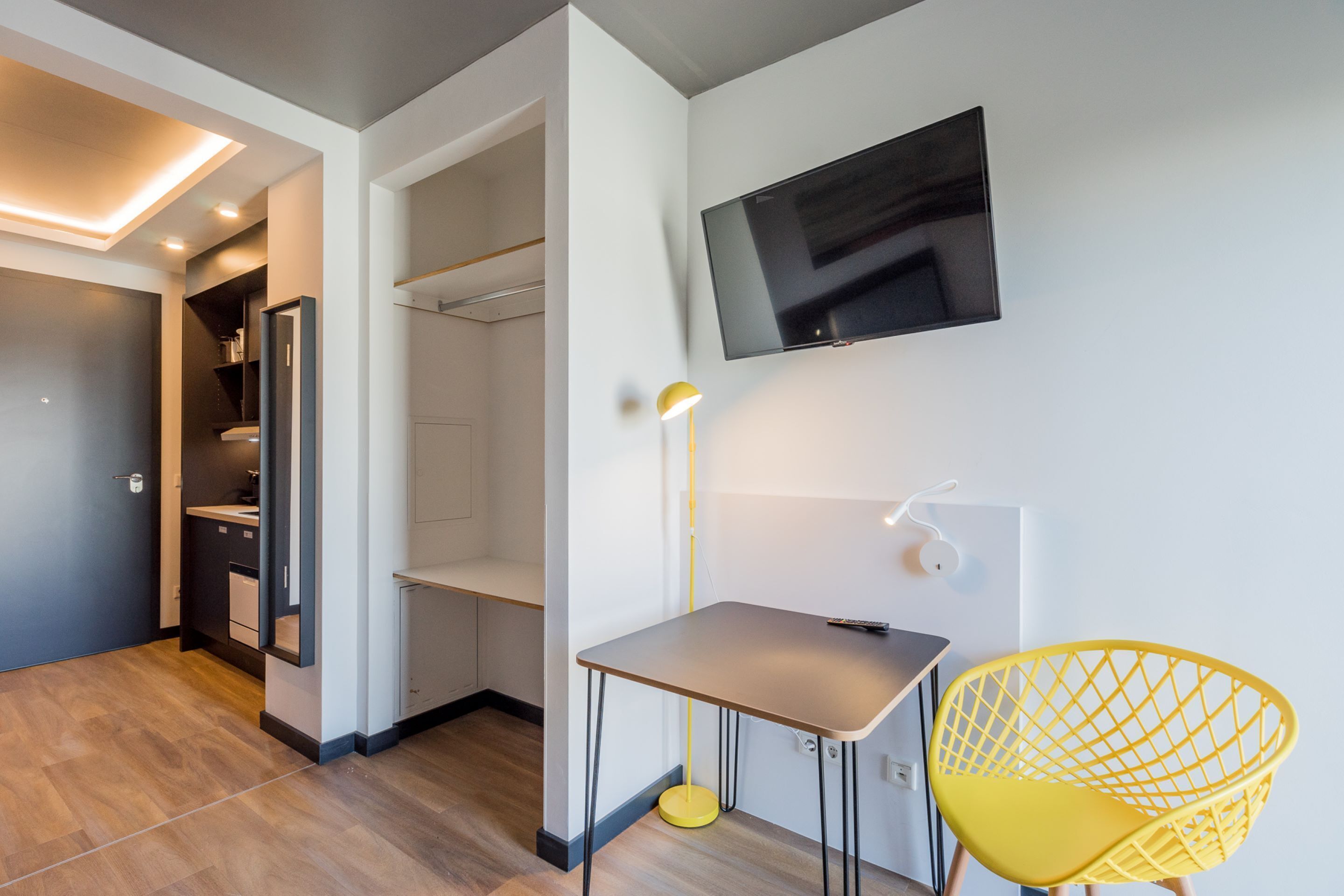 Een moderne hotelkamer met een flatscreen televisie aan de muur, een klein tafeltje met een stoel en een inloopkast.