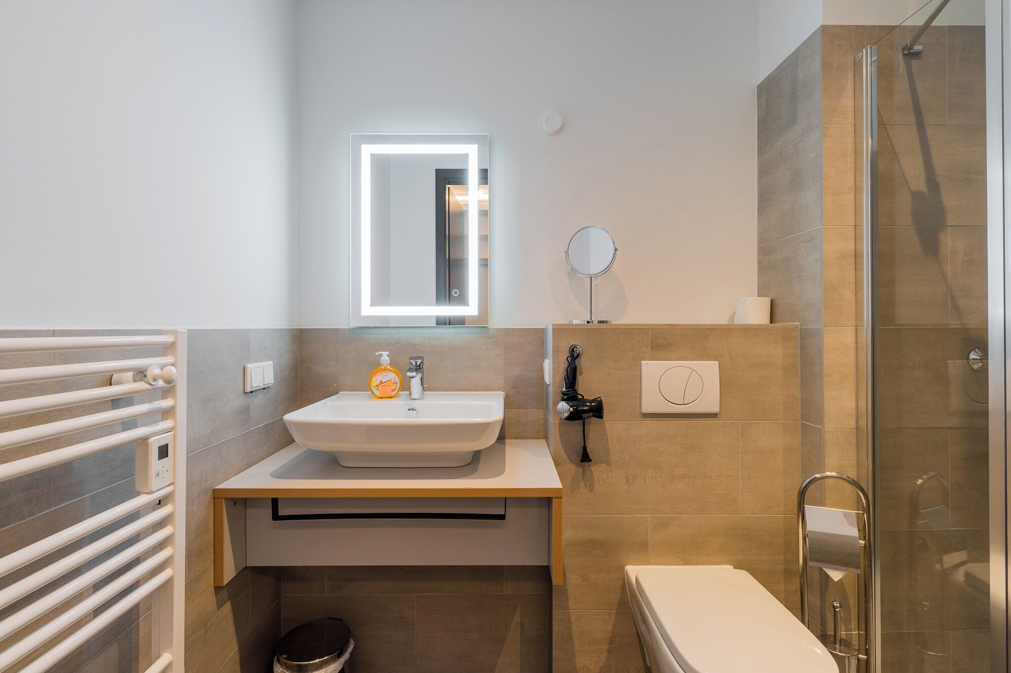 Un baño moderno con un lavamanos blanco, un espejo, un cabezal de ducha manual y un inodoro.