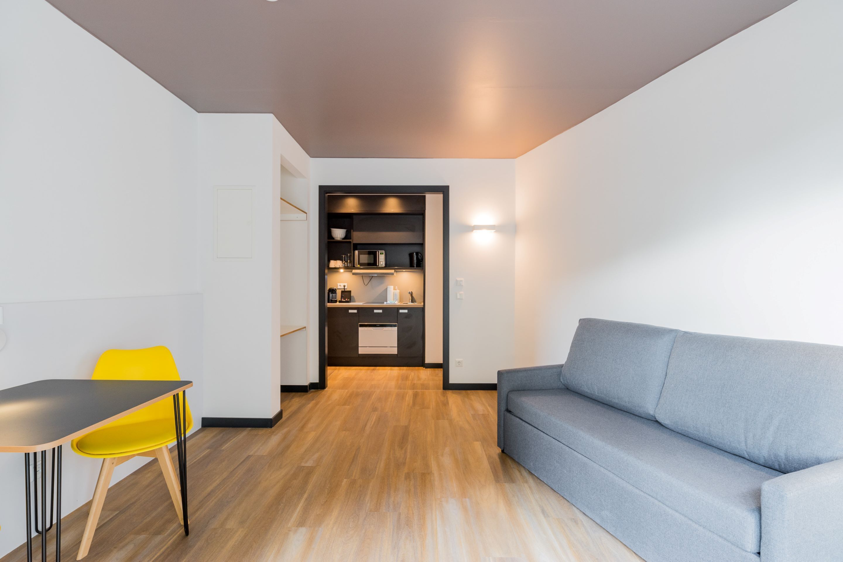 A compact living space with a kitchenette, a sofa, a dining table, and a bright yellow chair.