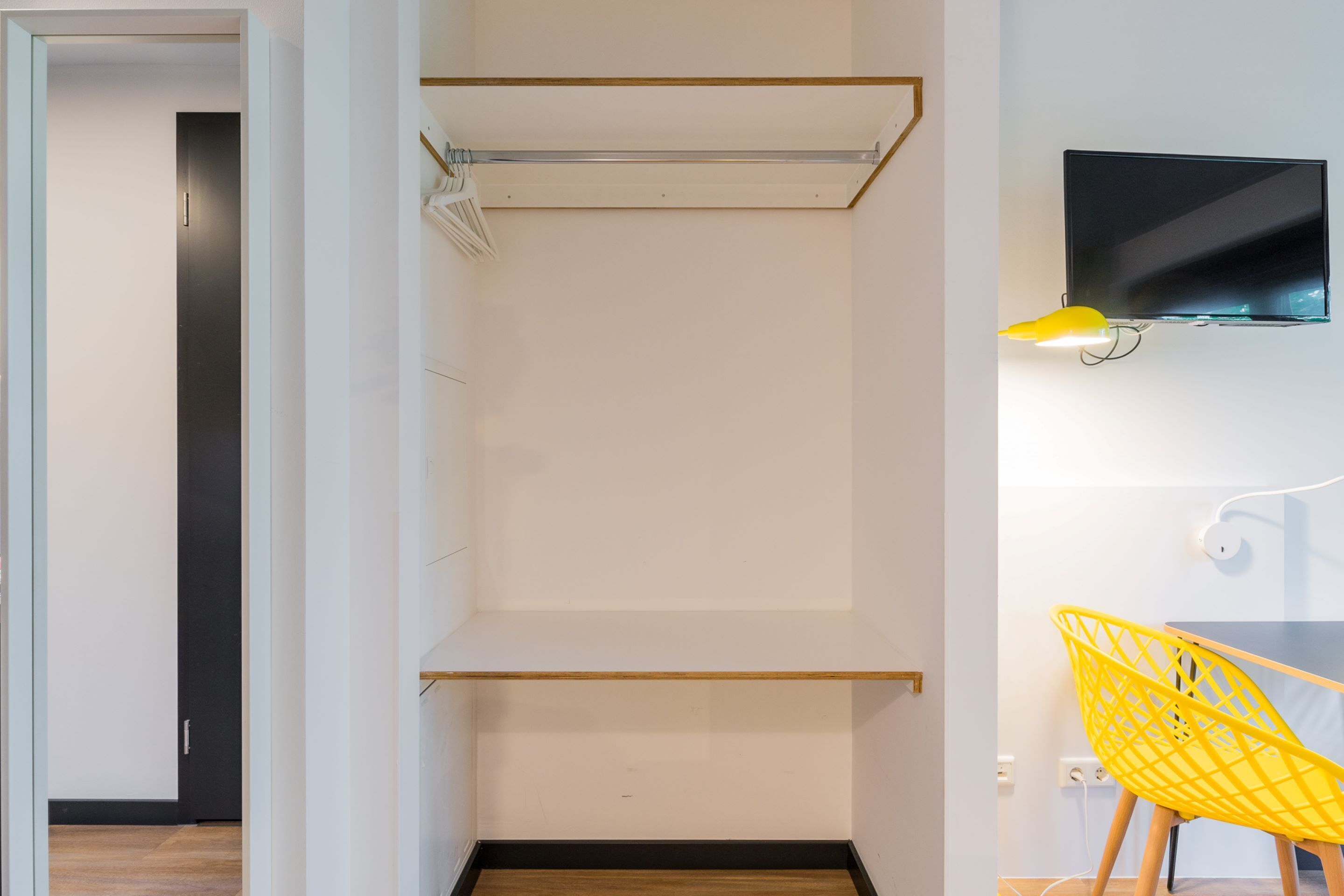Una habitación moderna con un televisor montado en la pared, una silla amarilla y piso de madera.