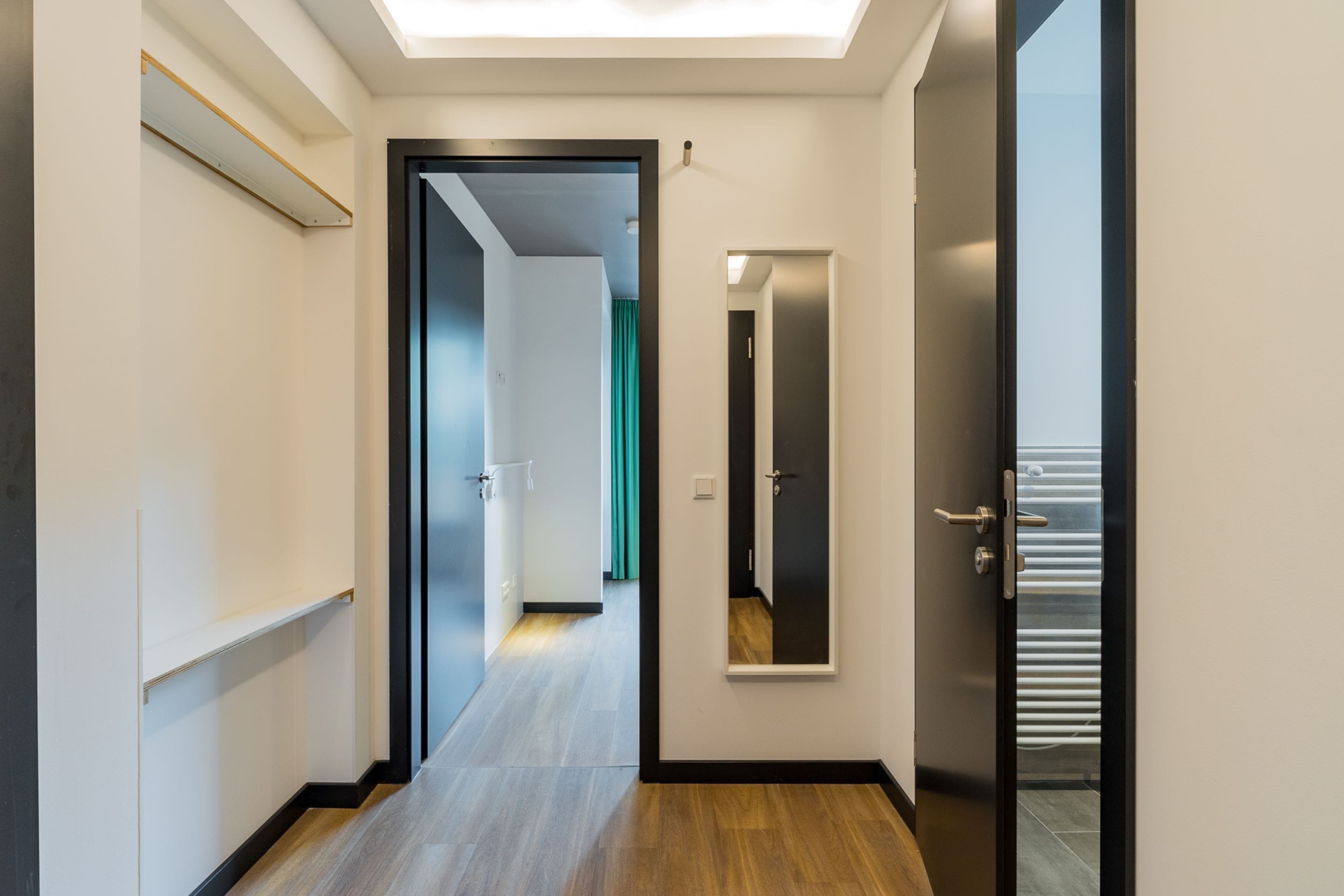 Um corredor com piso de madeira, um espelho com moldura preta e uma porta que dá para outro quarto.