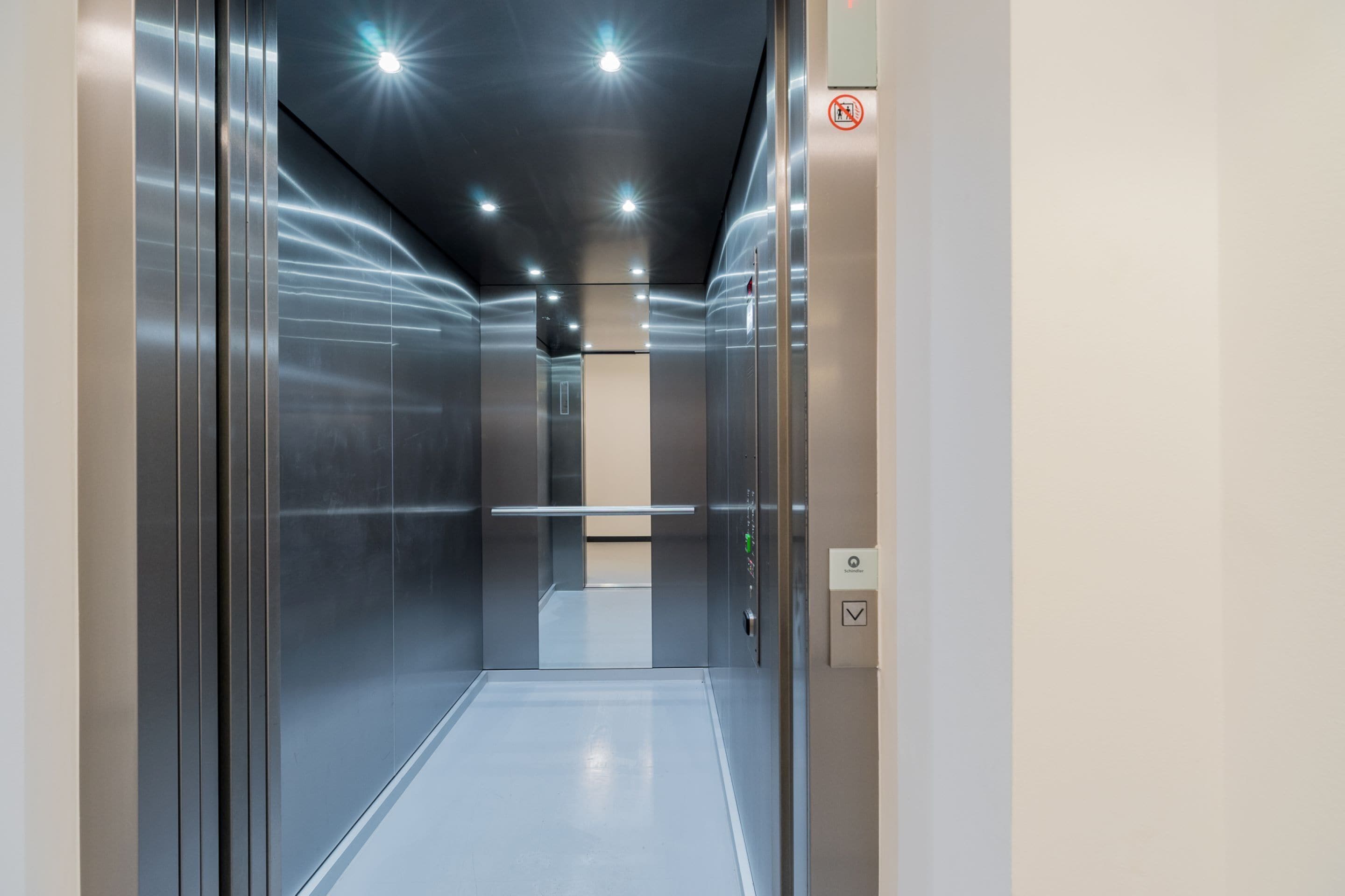 An elevator with metallic walls, a reflective floor, and a control panel with a green button.