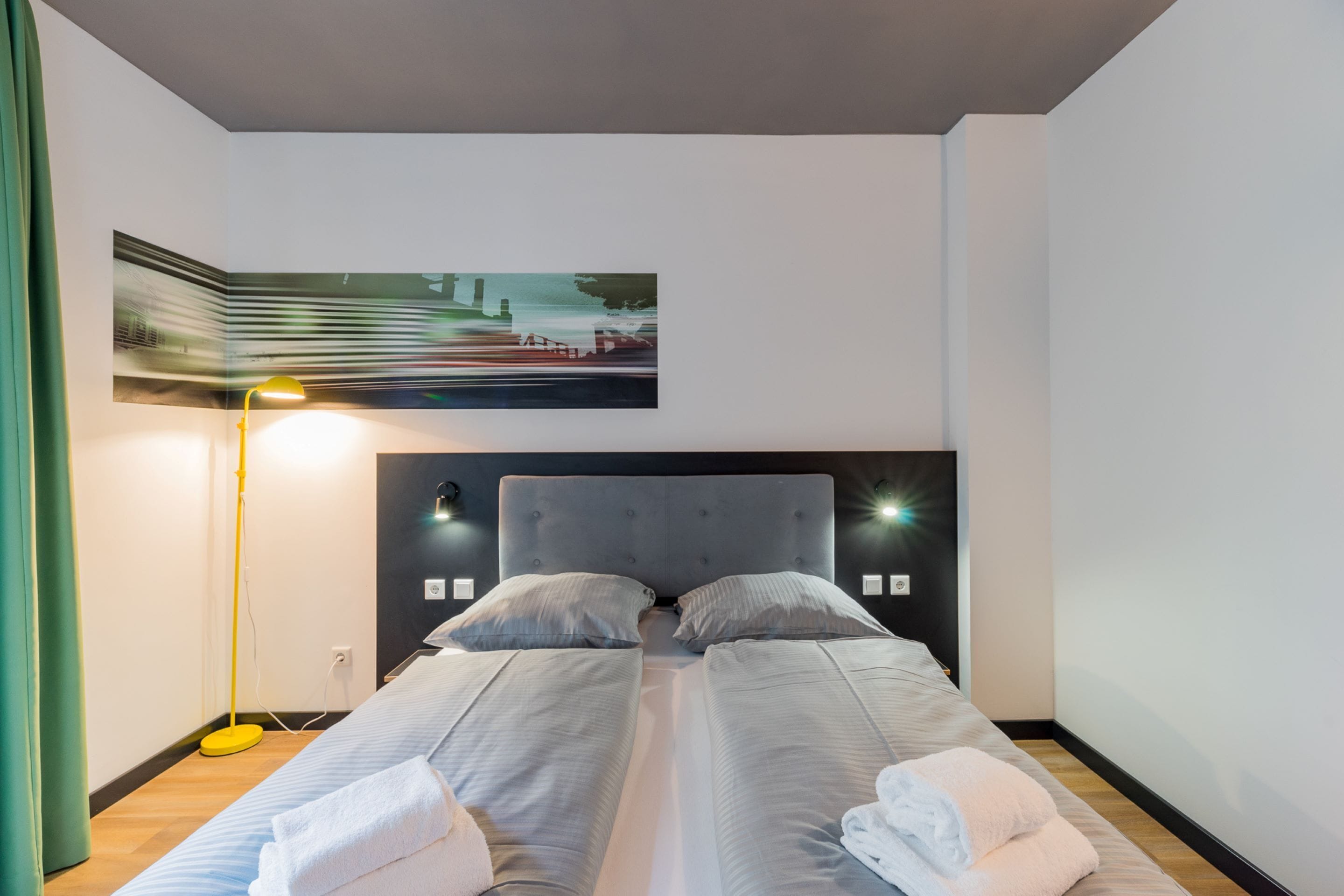 Una camera d'albergo con un letto matrimoniale, due comodini, una lampada da terra e un quadro appeso al muro.