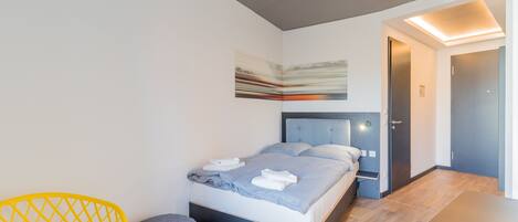 A modern hotel room with a bed, a small table, a chair, and a door.