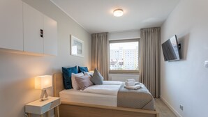 Et moderne hotelværelse med seng, sengebord, lampe og et fjernsyn ophængt på væggen.