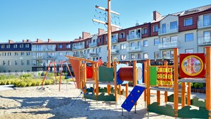 En legeplads med forskellige legekonstruktioner, blandt andet en rutchebane og klatreområder, foran boligbygninger.