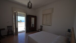 Ein Schlafzimmer mit Bett, einem Holzschrank, einem Stuhl und einer Tür zum Balkon.