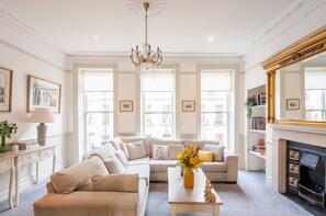 A spacious living room with a beige sofa set, a chandelier, a fireplace, and large windows. - Stunning Central Townhouse-Roman Baths- 3 min walk (Bath)