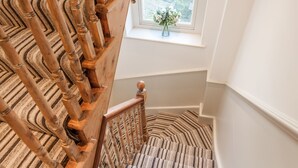 Una escalera de madera con alfombra a rayas que lleva a una ventana con un jarrón de flores.