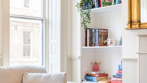 Una sala de estar acogedora con un sofá, una estantería llena de libros y una ventana que da a un edificio.