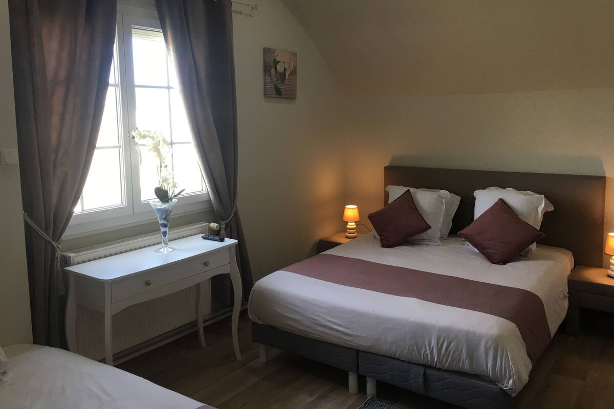 Een slaapkamer met een bed, nachtkastjes, een bureau en een raam met gordijnen.