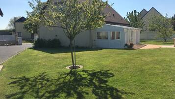 A residential house with a well-maintained lawn, a small tree, and a clear sky.