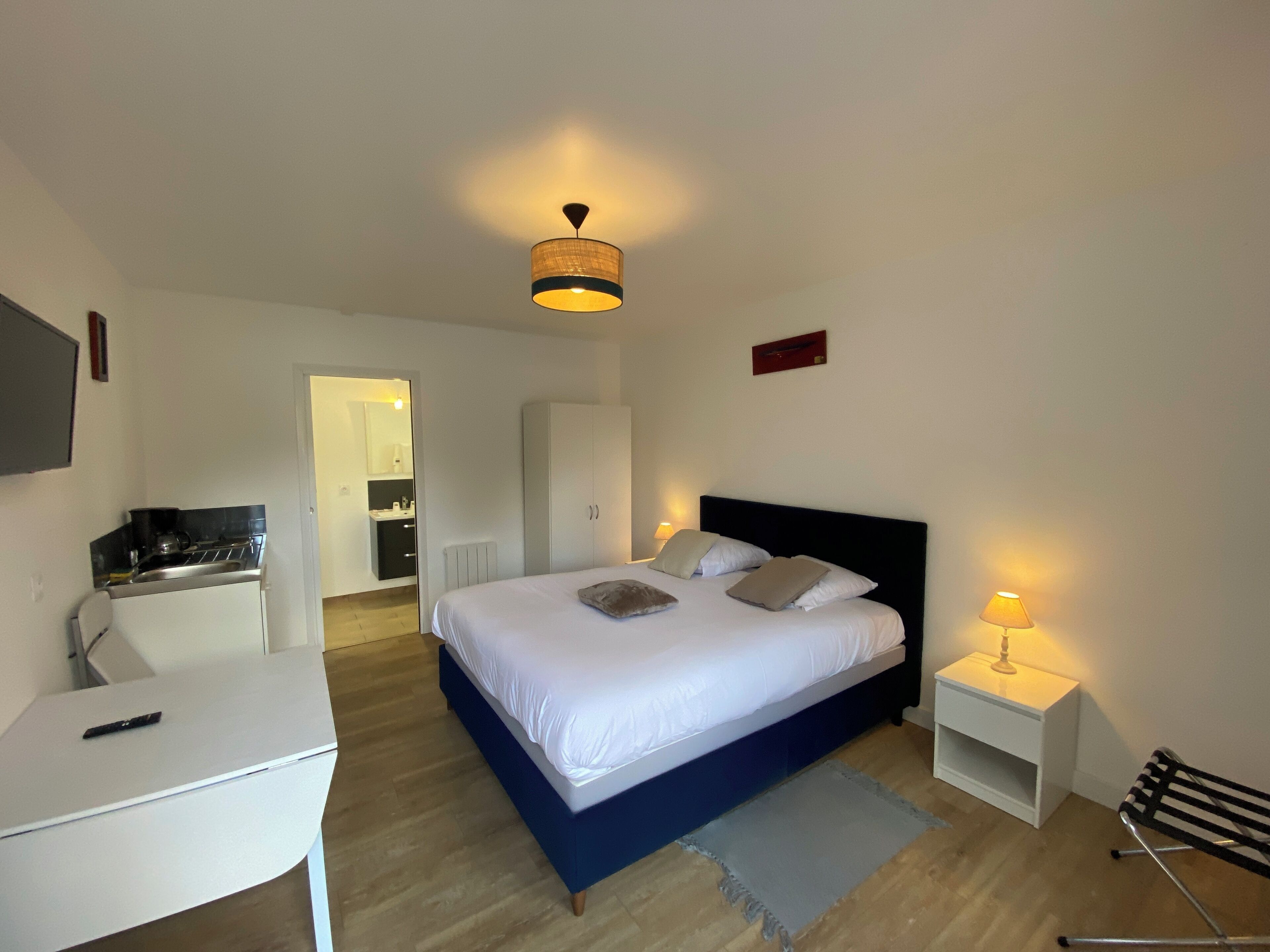 Un dormitorio con cama, mesitas de noche, escritorio y kitchenette.