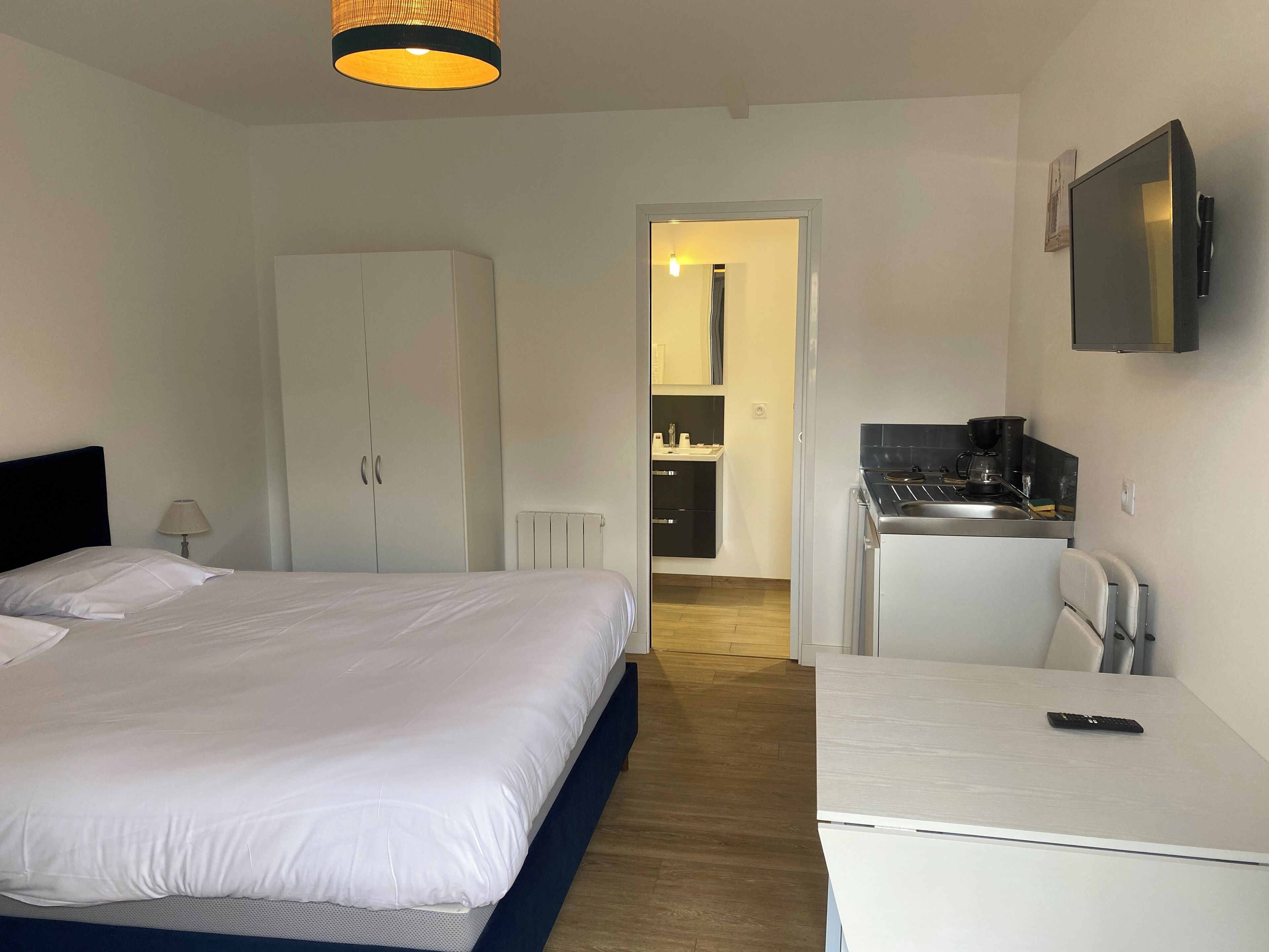 Een hotelkamer met een bed, een bureau, een stoel, een kitchenette en een kledingkast.