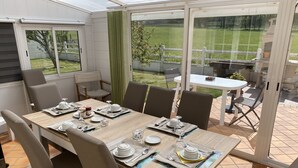 Ein Wintergarten mit einem Esstisch, gedeckt für sechs Personen, umgeben von Stühlen und Blick auf einen Rasen durch große Glasüren.